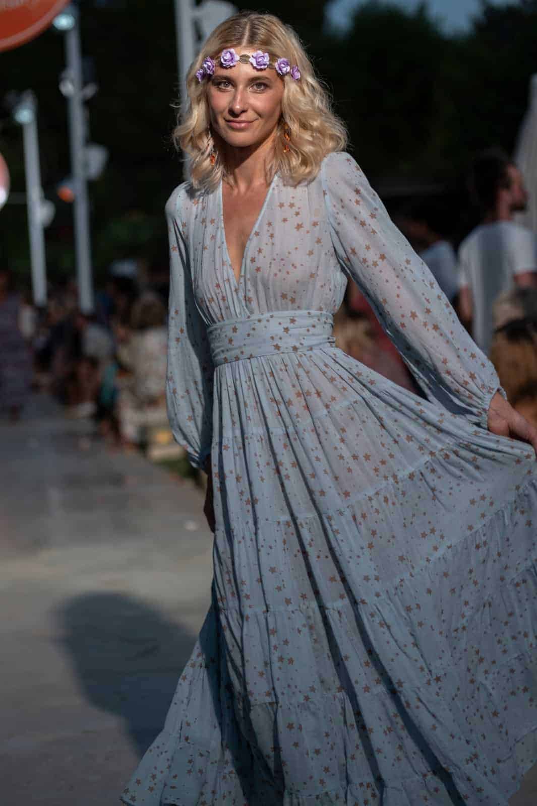 A stylish woman wearing a star-patterned dress with a floral headband at La Galeria Elefante Ibiza - Atzaro fashion show Ibiza, a vibrant outdoor art and cultural space.
