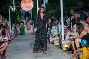 Elegant fashion model wearing a black and white boho dress walking runway at La Galeria Elefante Ibiza - Atzaro fashion show Ibiza, vibrant event scene.