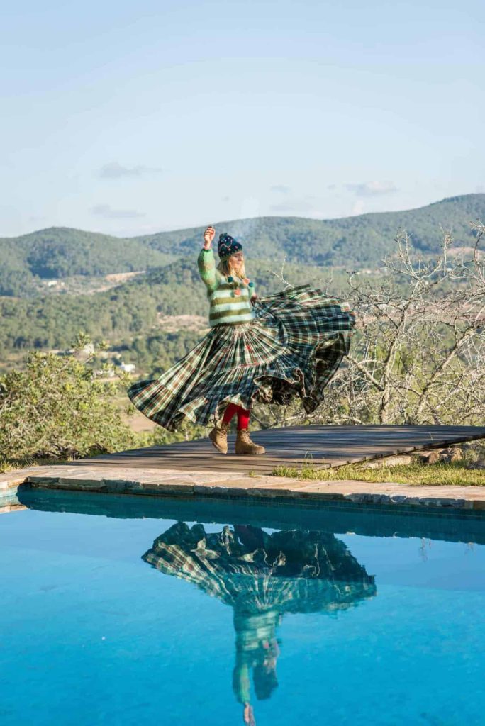 Vibrant woman in a green plaid skirt and cozy sweater performing dance near a pool.