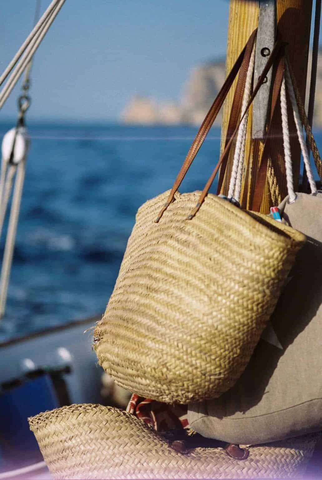 Image depicts a straw tote bag hanging on a boat with a scenic ocean background, for La galeria elefante