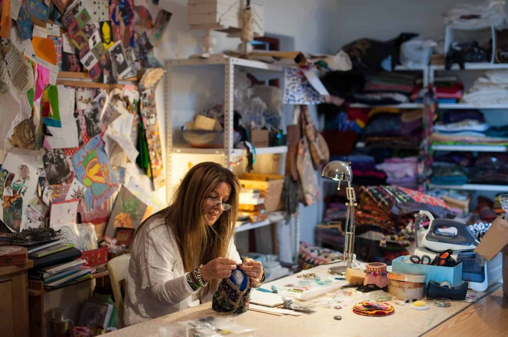 An artistic studio at La Galeria Elefante featuring textiles, artwork, and jewelry crafts with a woman creating handmade jewelry.