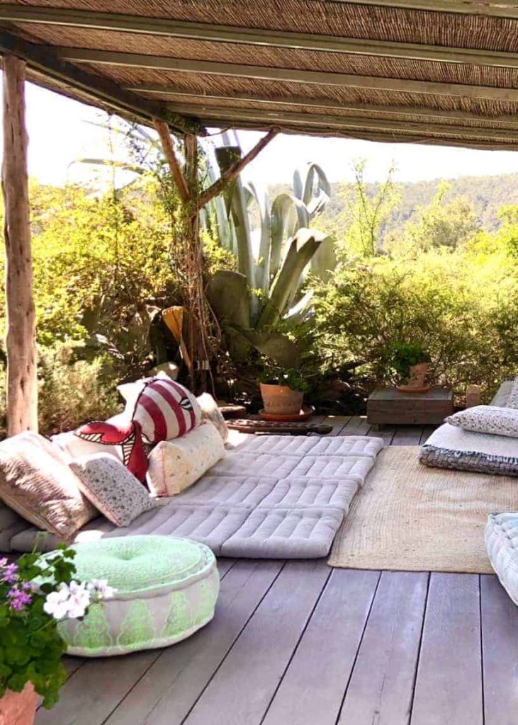 A cozy outdoor lounging area decorated with cushions, rugs, and abundant plants, creating a peaceful retreat in nature.