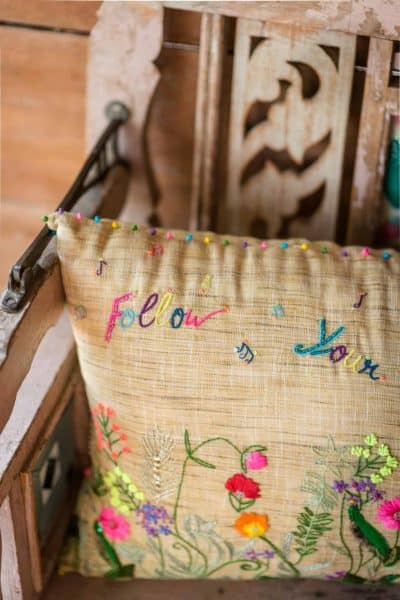 Close up of a cushion with floral embroidery and multicoloured French Knotting along the edge