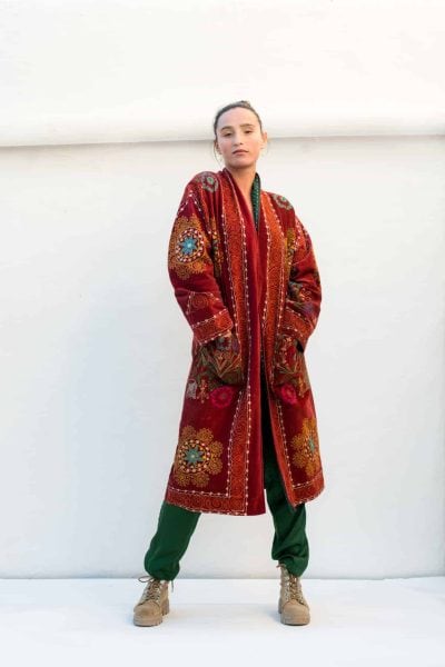 long rust coloured coat with embroidery and green trousers