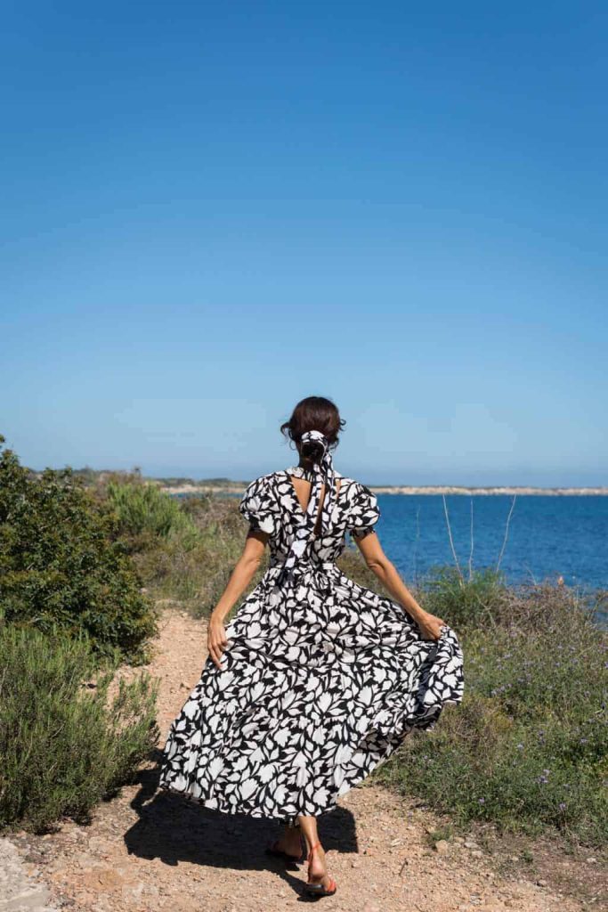 Beautiful woman in black and white floral dress walking on coastal trail with sea view for La Galeria Elefante, stylish beach fashion and scenic landscape.