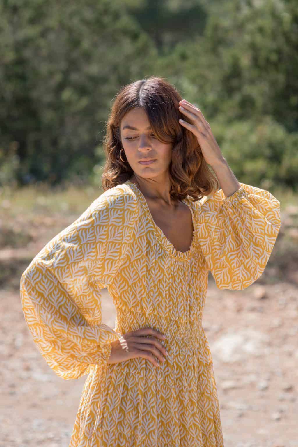 Elegant woman in yellow patterned dress at La Galeria Elefante, enjoying outdoor setting, natural light, stylish fashion, vibrant colors, scenic background, summer vibe, boho clothing.