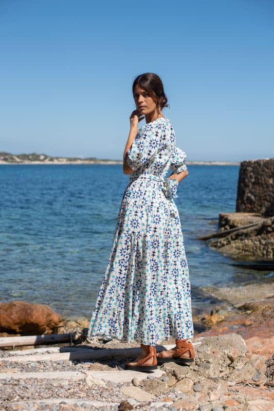 Elegant woman in a mosaic tile print maxi dress by the seaside, showcasing bohemian fashion and beachwear styles at for Galeria Elefante Ibiza.