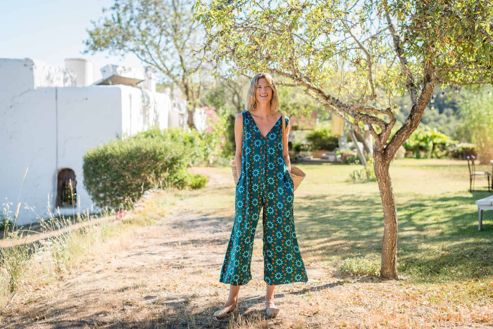 La Galeria Elefante Ibiza Woman in vibrant bohemian jumpsuit standing outdoors in Ibiza with trees and greenery.