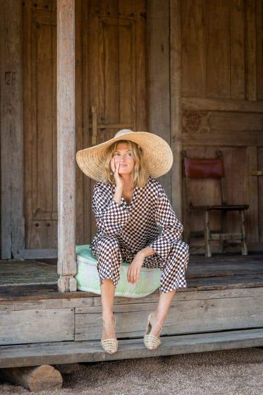 La Galeria Elefante Ibiza Woman in bohemian outfit with large straw hat sitting on wooden porch in Ibiza.