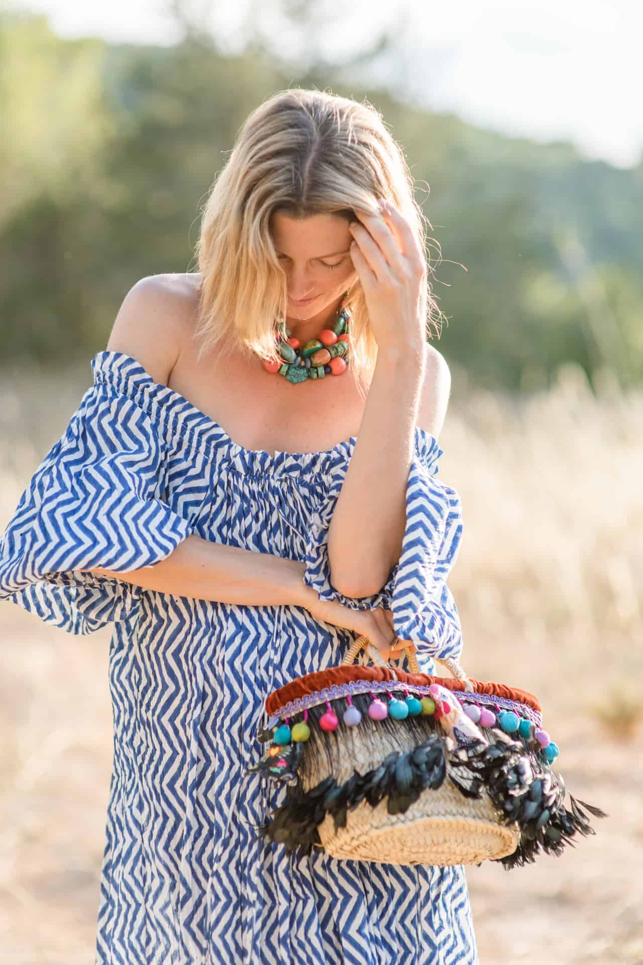 Colorful woven handbag with feathers and pom-poms, boho style, outdoor setting, summer fashion, accessories, casual wear, beach bag, artisan crafted, vibrant textiles, unique style by La Galeria Elefante