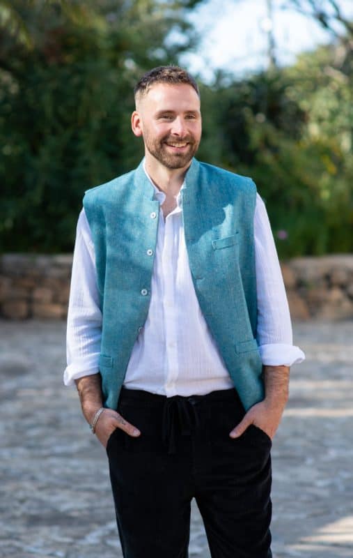 Model wearing a blue waistcoat over a white shirt with black cord trousers