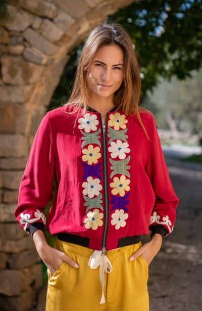 Model wears a red silk embroidered jacket with yellow modal trousers in a garden