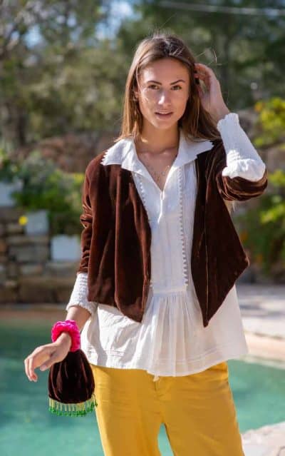 Model wearing a brown velvet jacket with a white top yellow trousers and a small velvet bag