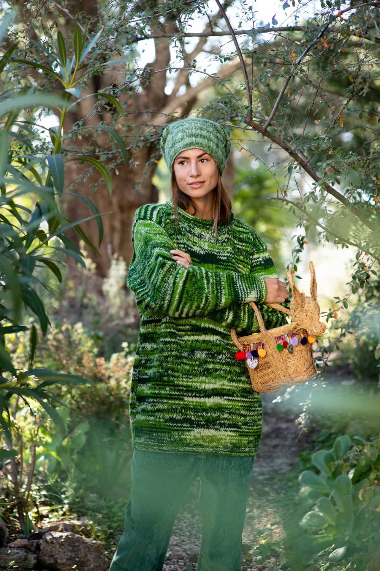 Model wears a green woolly jumper with green corduroy trousers and a green woolly beanie in a garden