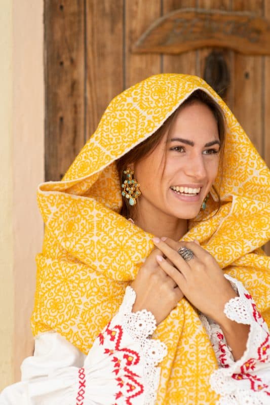 Close up of model wearing a yellow embroidered wool shawl with a vintage white red and yellow blouse and turquoise earrings
