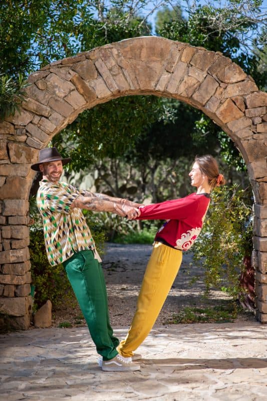 Models wearing matching modal trousers in yellow and green holding hands in a garden
