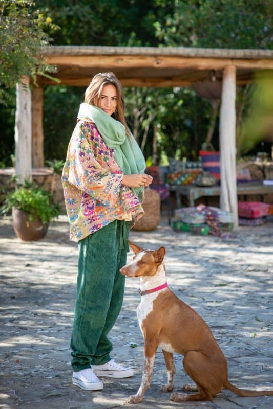 Model in a garden wearing green cord trousers with a multicoloured jacket and a green cashmere scarf profile
