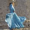 Model wears a floor length turquoise floral block print dress with long sleeves and a straw hat profile