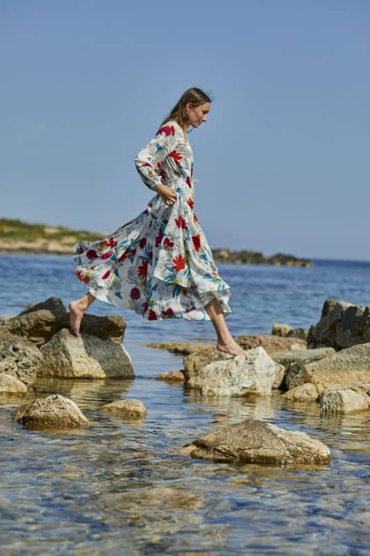 Model wearing a white floral floor length dress with long sleeves by the sea profile