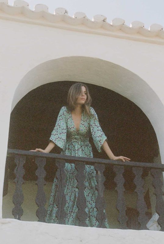 Model wearing floor length kimono style turquoise block print silk dress with a V neck on a balcony
