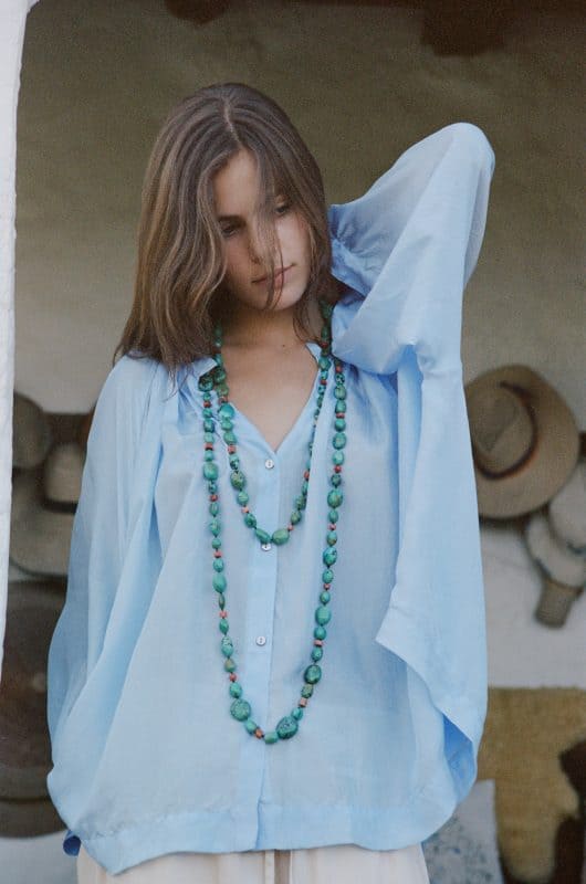 Model wearing a sky blue silk blouse and a long turquoise necklace close up