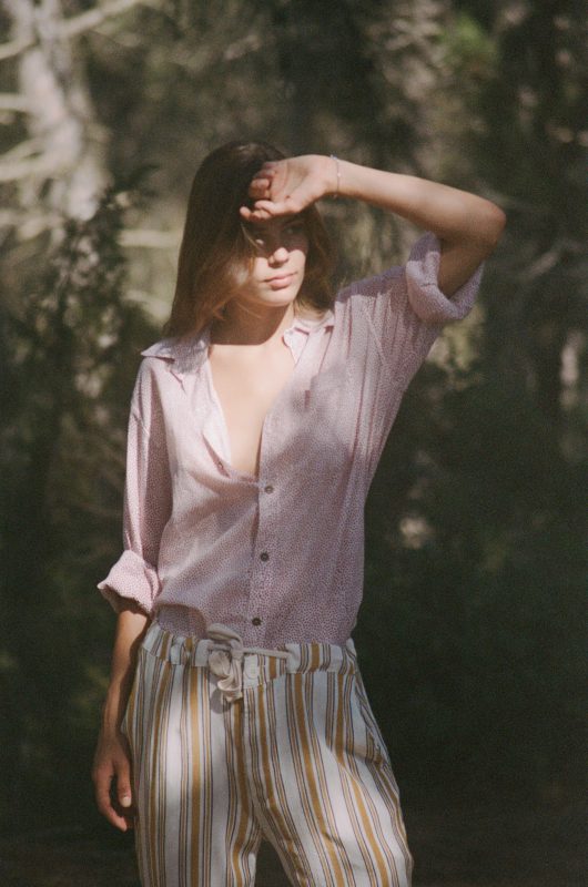 Model in a forest wearing white and yellow striped trousers and a cotton hand block print shirt with red dots