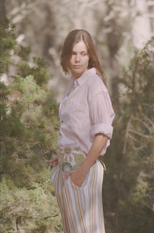Model wears a cotton red dots hand block print shirt with white and yellow striped trousers and a multicoloured belt in a forest profile