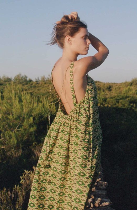 Model wears a strappy open back floor length cotton dress in a green print back view