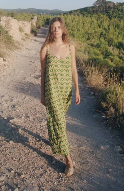 Model wears a floor length strappy cotton dress in a green print in a field