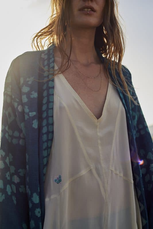 Close up of a model wearing a cream crepe silk butterfly embroidered slip dress with an indigo kantha jacket