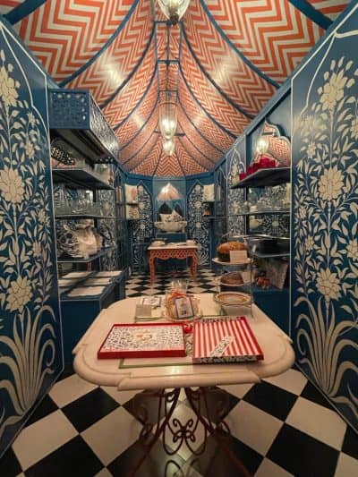 Cozy interior of a store featuring vibrant blue walls, elegant shelves with decorative items, and white table with red adn white stripey trays, flowers are apinted on teh walls