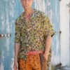 A vibrant image of a man wearing Jerome Shorts in Kantha, featuring colorful, patterned shorts and a matching shirt, standing outdoors against a rustic, weathered wall.
