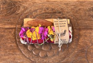Mini Sahumo & Palo Santo set with colorful flower petals on a rustic wooden surface, used for spiritual cleansing and aromatic rituals, featured in La Galeria Elefante.