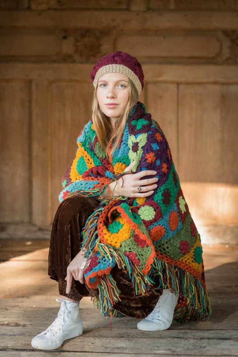 Girl with blonde hair wearing a colourful knitted poncho with a burgandy beany hat