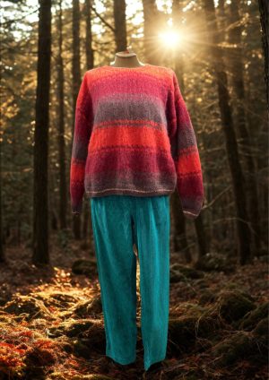 A cozy, colorful sweater with red, pink, gray, and orange stripes paired with bright turquoise pants, displayed outdoors in a sunlit forest setting.