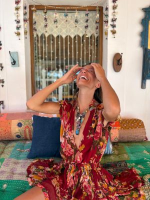 La Galeria Elefante Ibiza Woman in vibrant bohemian dress laughing in colorful Ibiza boutique setting with handmade decor.