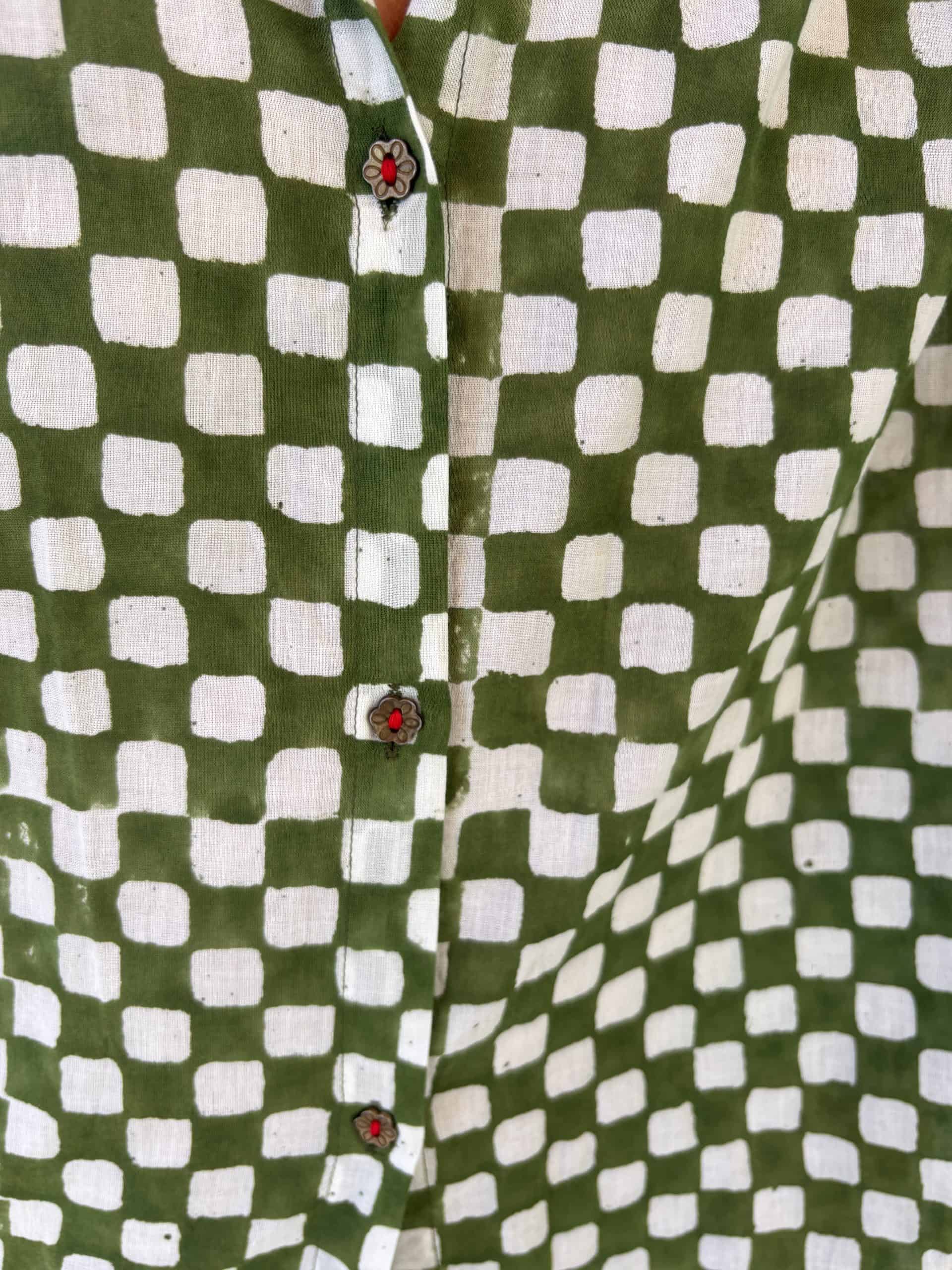La Galeria Elefante Ibiza Close-up of green and white checkered artisan fabric shirt with ladybug buttons.