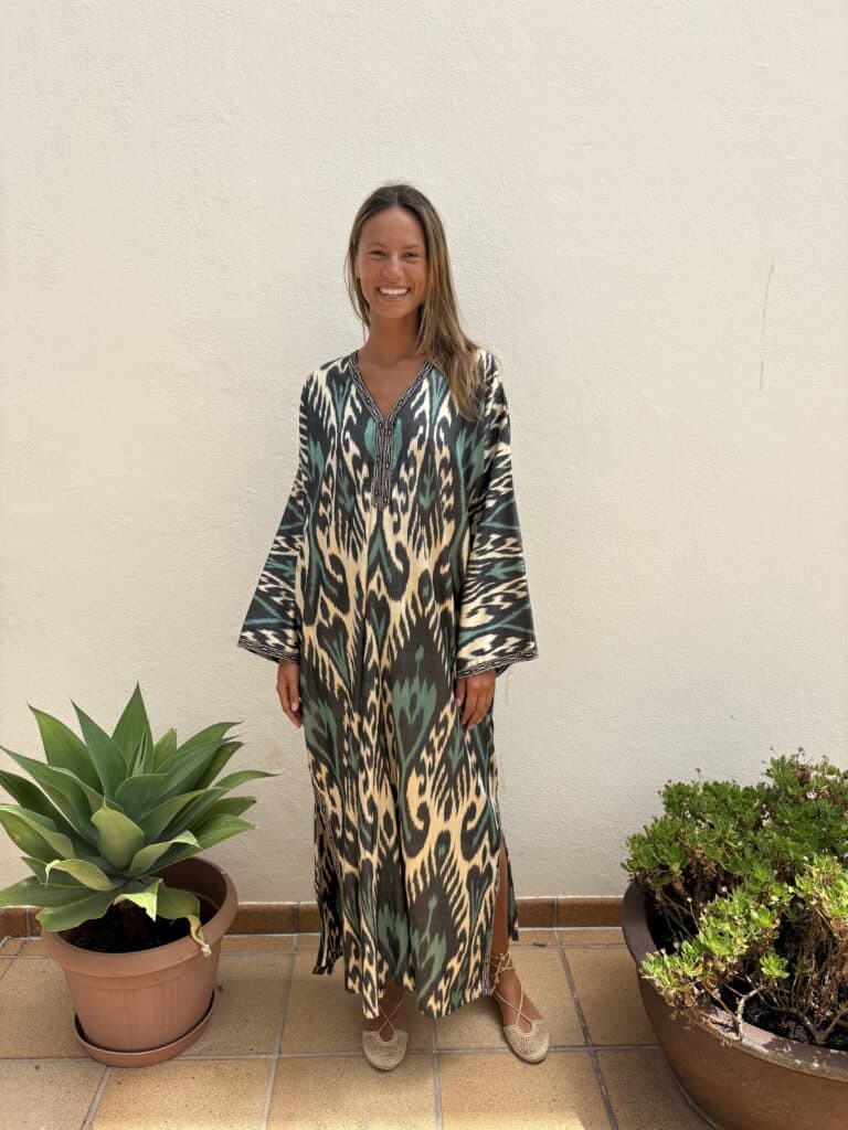 La Galeria Elefante Ibiza Woman in bohemian dress with vibrant Ikat pattern, standing outdoors with potted plants.