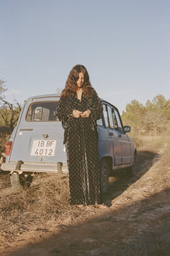 La Galeria Elefante Ibiza Woman in bohemian dress standing beside vintage car in Ibiza countryside.